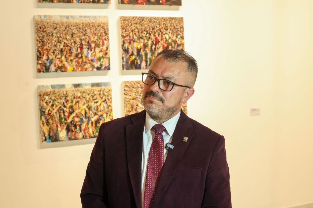 José Guadalupe Miranda Hernández, secretario de Centros Universitarios y Unidades Académicas Profesionales de la UAEMéx, presenta información sobre la transformación de unidades académicas en centros universitarios, con obras de arte abstracto en el fondo.