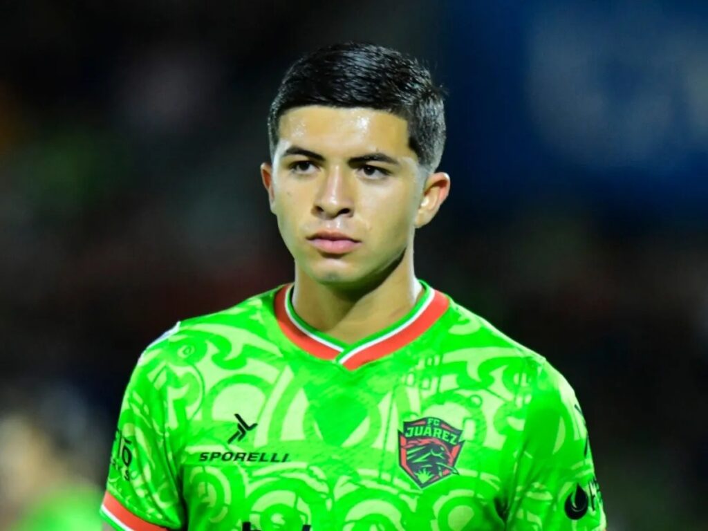 Retrato de Denzell García, jugador de fútbol del FC Juárez, vistiendo un uniforme verde con diseño y el logo del club, en un ambiente de partido.