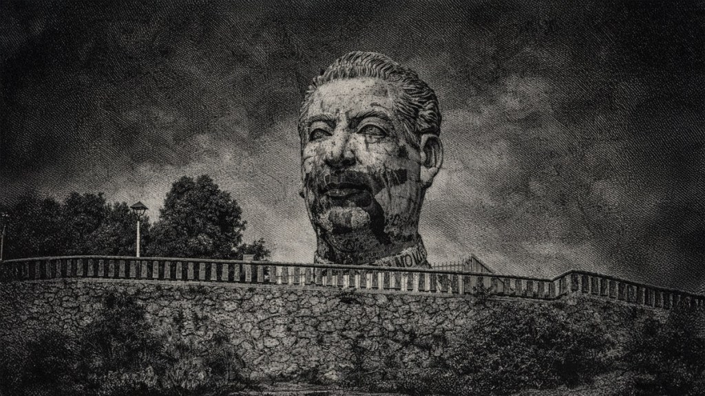 Retrato en blanco y negro de una estatua grande de un hombre, situada en un muro de piedra con un fondo nublado.