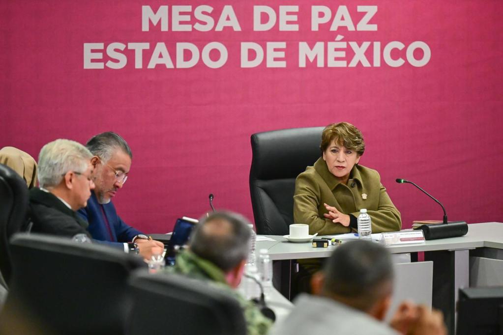 Reunión de la Mesa de Paz en el Estado de México, donde se discuten temas de seguridad. Se observan a varios funcionarios, con un enfoque en una mujer que habla al micrófono.