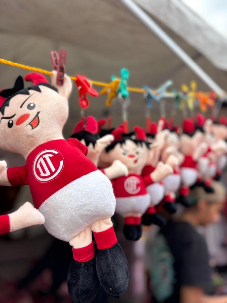 Peluches del equipo Diablos Rojos colgados en una cuerda, decorando un ambiente festivo previo a la gran final.