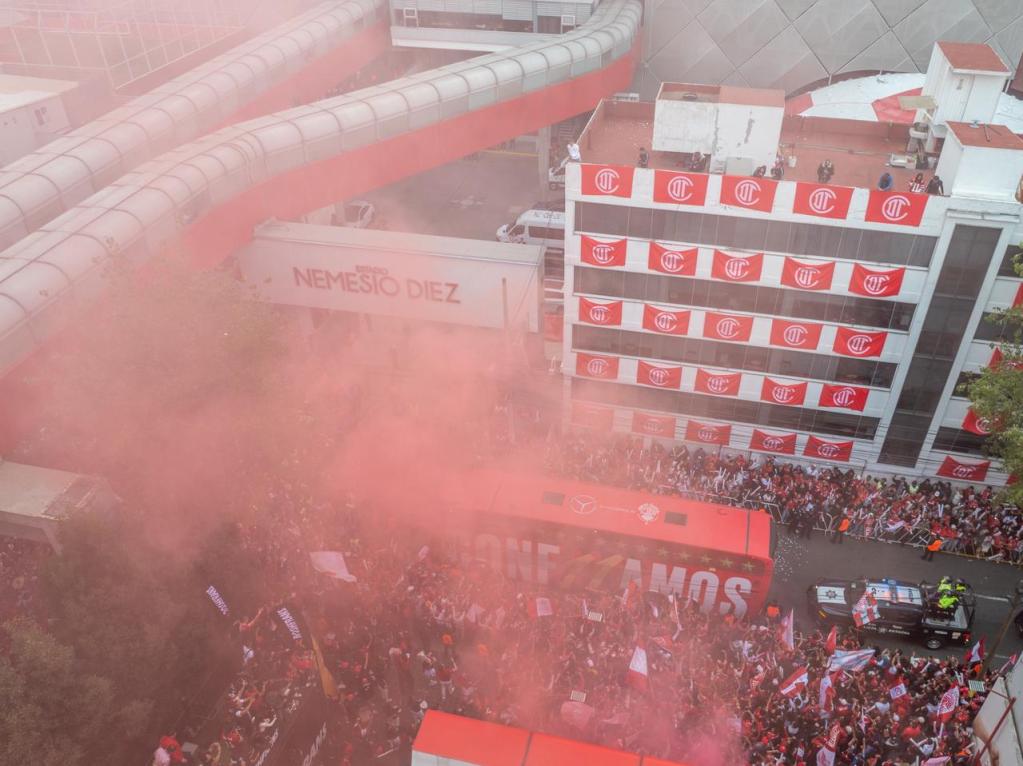 Vista aérea del Estadio Nemesio Diez con una multitud de aficionados del Toluca FC reunidos y celebrando, rodeados de humo rosa y banderas del equipo.