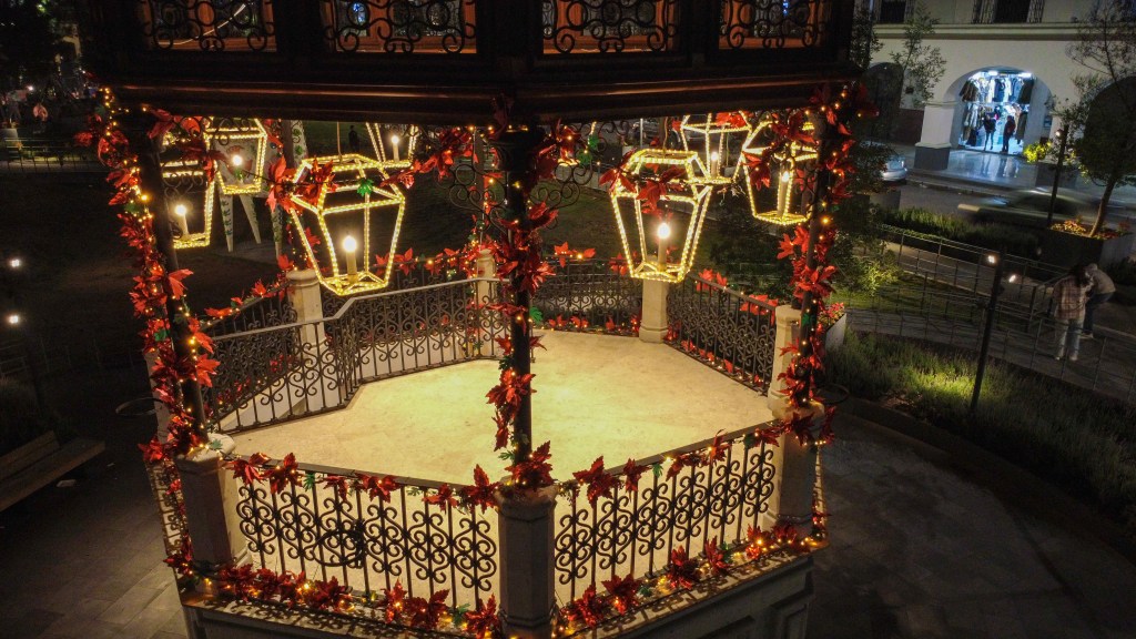 Kiosko navideño decorado con luces y adornos festivos, rodeado de nochebuenas, en un ambiente romántico y acogedor durante la temporada navideña.