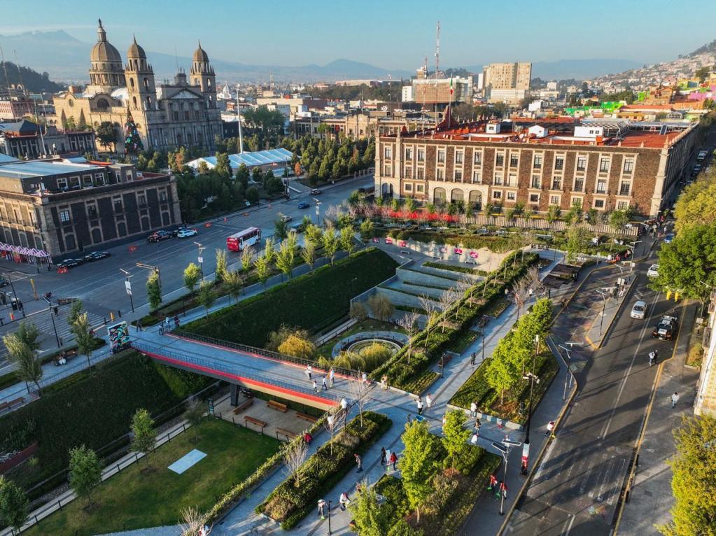 Vista aérea del centro de la capital mexiquense, mostrando espacios verdes, una plaza, edificios emblemáticos, y personas caminando.
