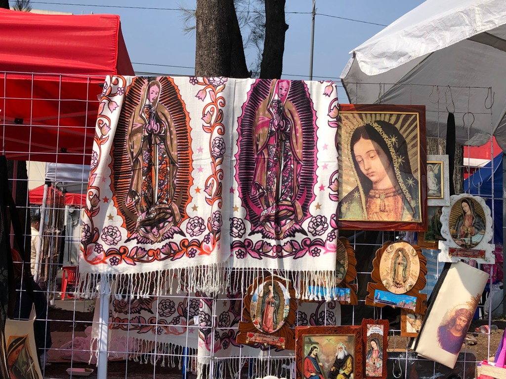 Varios artículos religiosos, incluyendo mantas y estampas de la Virgen de Guadalupe, expuestos en un mercado al aire libre durante la festividad del 12 de diciembre.