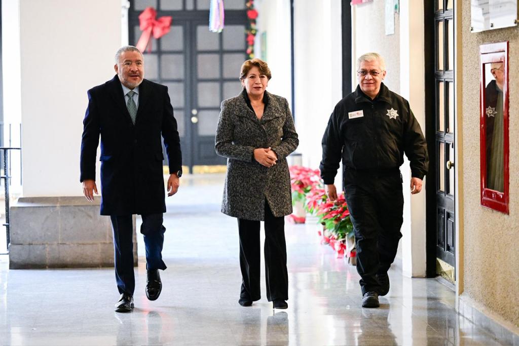 Tres personas caminando por un pasillo decorado con plantas, en un entorno institucional.