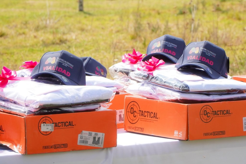 Uniformes nuevos y gorras con el logo de la Coordinación de Vialidad de Mexicaltzingo, apilados en cajas naranjas con cintas rosas, sobre una mesa al aire libre.