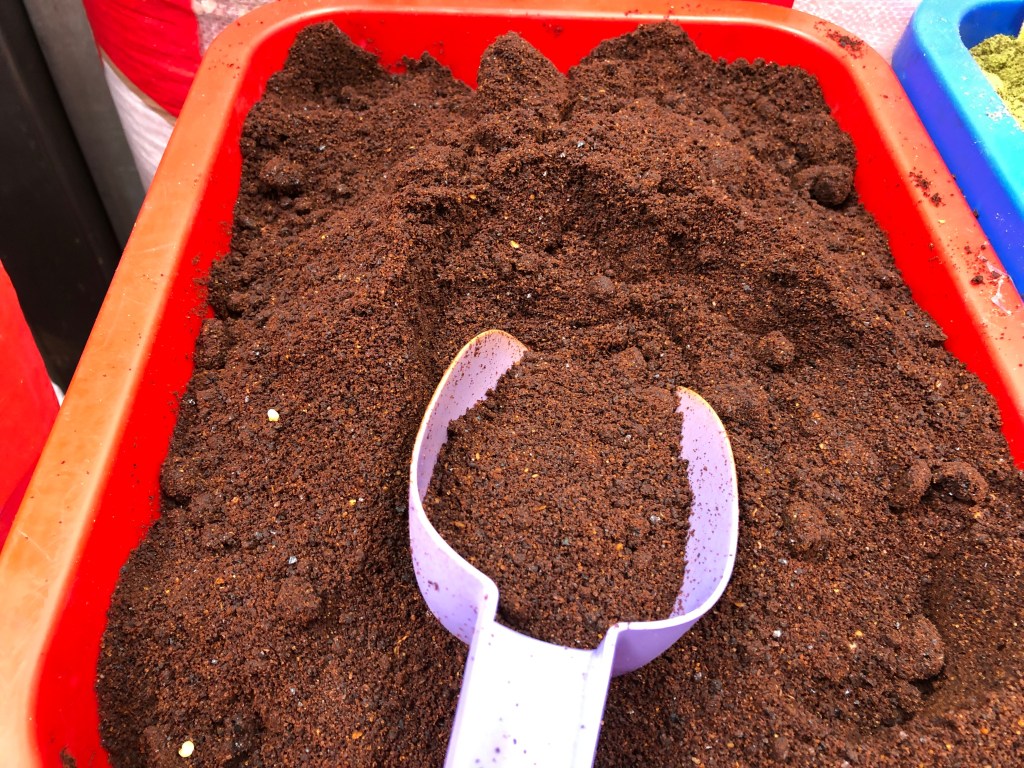 Caja con polvo de especias o café, con una cuchara de plástico apoyada sobre la superficie.