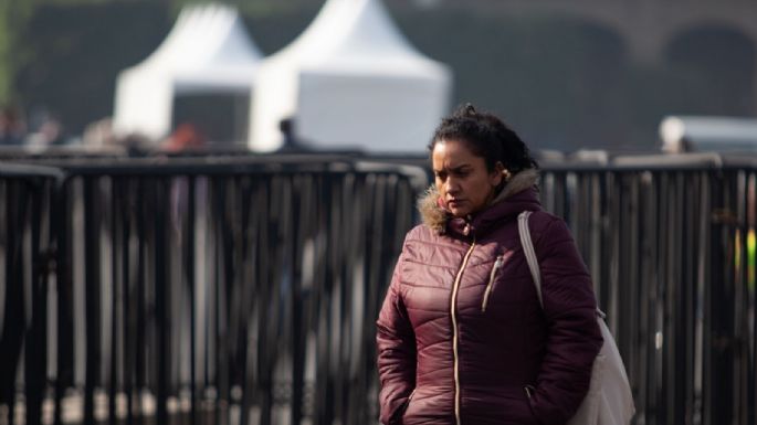 Mujer con abrigo morado caminando en un área pública con carpa al fondo en un día frío.