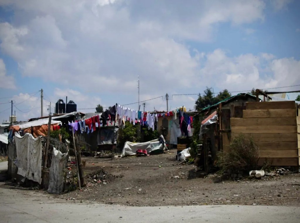 Vista de un asentamiento precario con casas en mal estado y ropa colgada en cuerdas, mostrando las difíciles condiciones de vida en una zona rural.