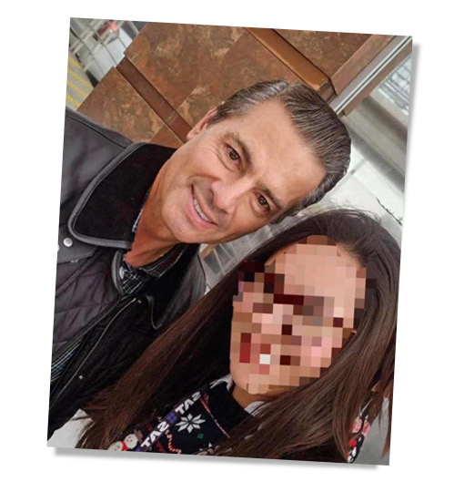 Selfie de un hombre sonriente con cabello corto y chaqueta oscura, junto a una mujer con el rostro pixelado. Ambos parecen estar en un lugar público.