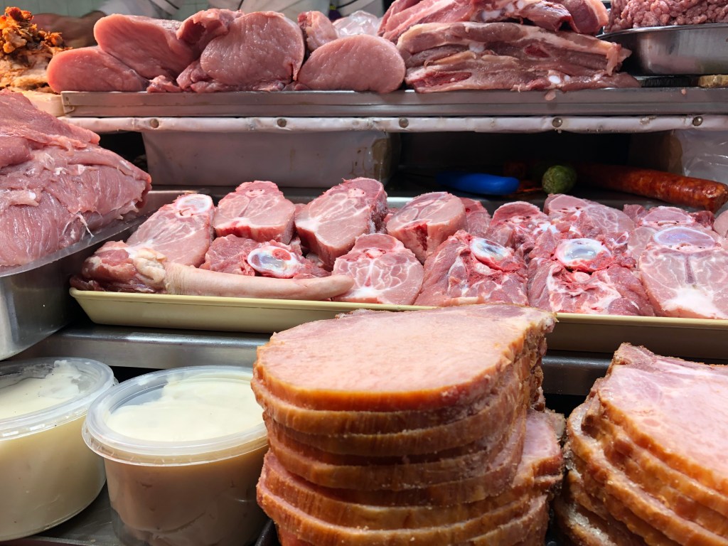 Carnes frescas exhibidas en un mercado, incluyendo cortes de cerdo y tocino en envases.