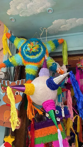 Una colorida colección de piñatas en un establecimiento, incluyendo una piñata de estrella con cintas brillantes y otra piñata esférica con picos y colores vibrantes.