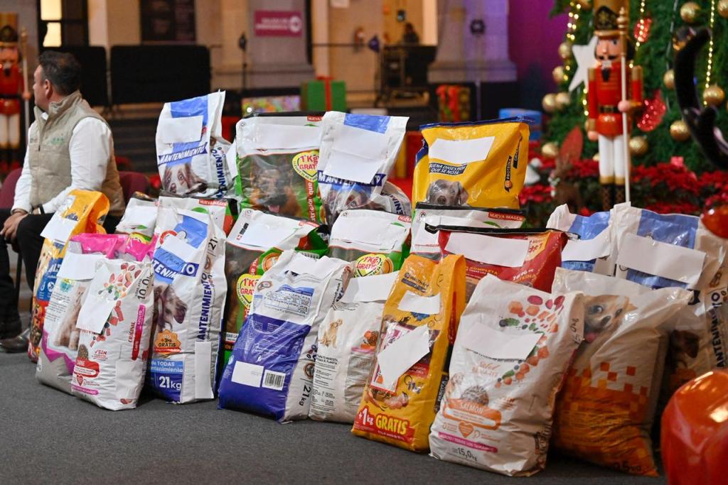 Un grupo de bolsas de alimento para perros apiladas en un evento benéfico, con un hombre sentado al fondo. El lugar está decorado con elementos festivos.