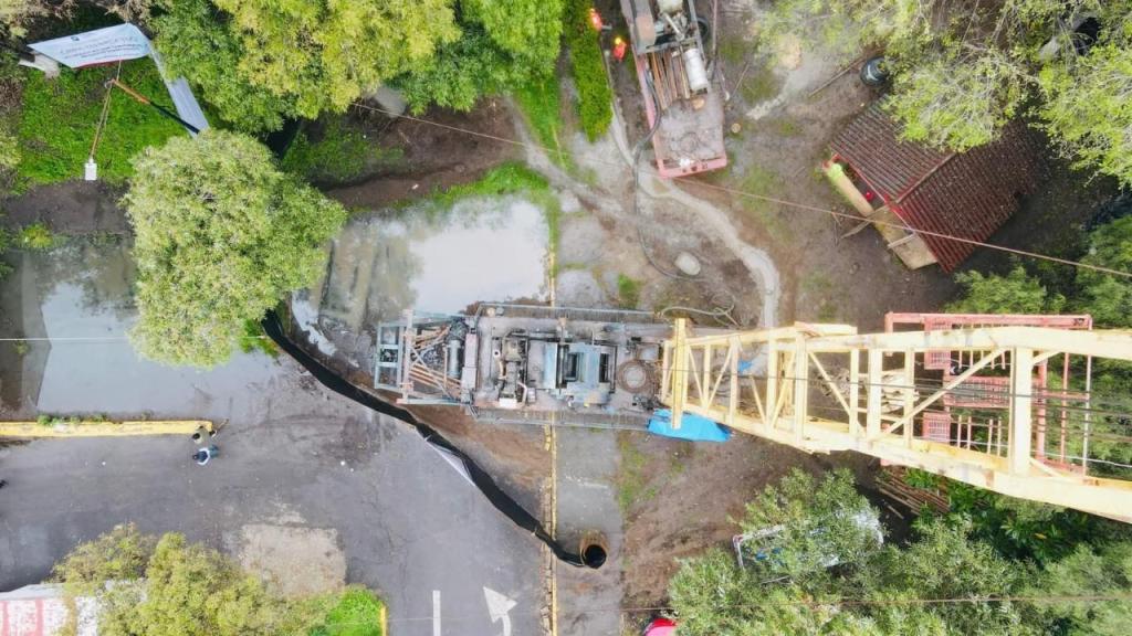 Vista aérea de un sitio de perforación de pozos de agua con maquinaria y equipo visible en una zona verde, rodeado de árboles y vegetación.