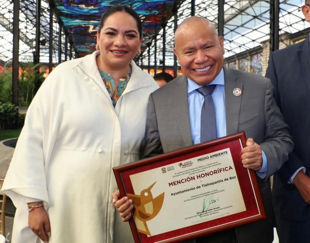 Una mujer y un hombre sonríen mientras sostienen un premio de reconocimiento honorífico por el trabajo del Ayuntamiento de Tlalnepantla en la promoción del medio ambiente.