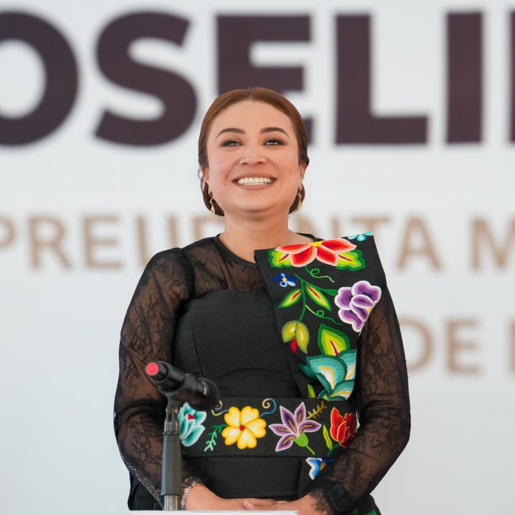 Yoselin Mendoza, alcaldesa de Nicolás Romero, sonríe mientras presenta su Primer Informe de Gobierno, luciendo un vestido negro con detalles coloridos, en un evento formal.