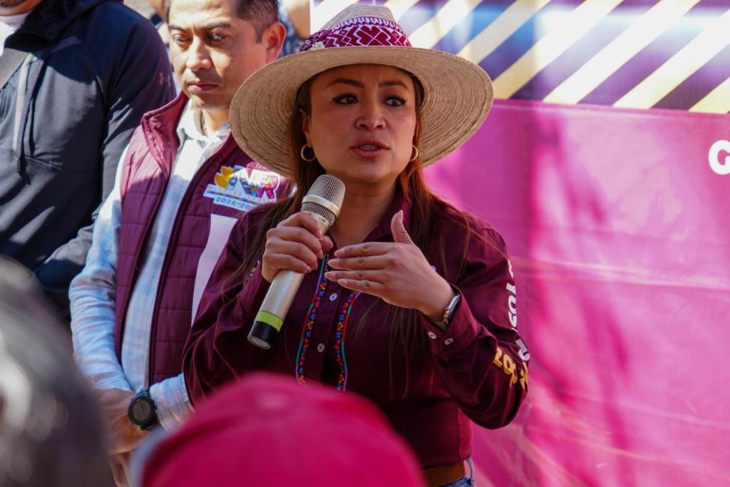 La alcaldesa Yoselin Mendoza hablando durante la inauguración de la repavimentación de la calle Revolución, vestida con una camisa tradicional y un sombrero, mientras sostiene un micrófono.