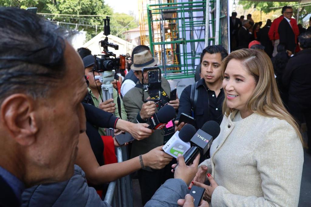 Una funcionaria municipal, Ana Muñiz Neyra, siendo entrevistada por varios reporteros durante un evento público, mientras sostiene un micrófono.