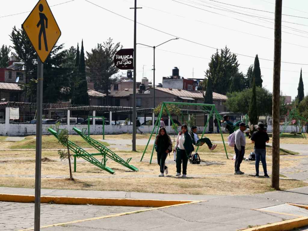 Vista de un parque en La Crespa Floresta, Toluca, con columpios y niños jugando, mientras adultos conversan en el área verde.