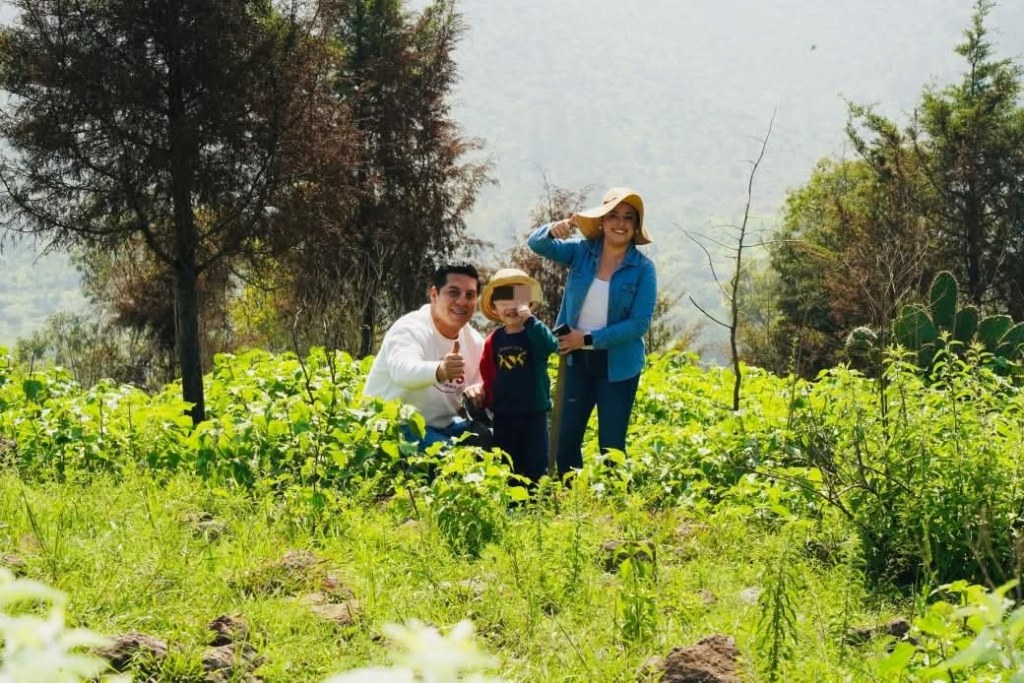 Una familia sonriente posando en un campo verde, rodeada de arbustos y árboles, disfrutando de un día en contacto con la naturaleza.