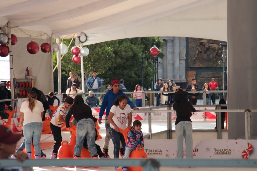 Grupo de personas patinando en una pista de hielo en Toluca, con un ambiente festivo y decoraciones navideñas.
