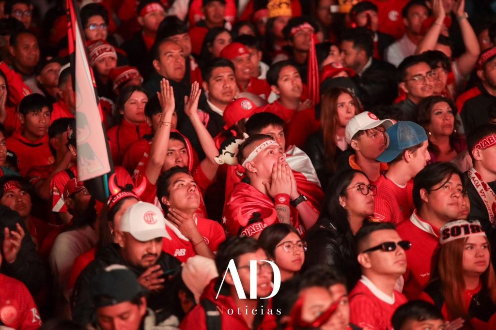 Aficionados de Toluca vestidas de rojo, mostrando emociones intensas mientras siguen un partido desde un lugar público.