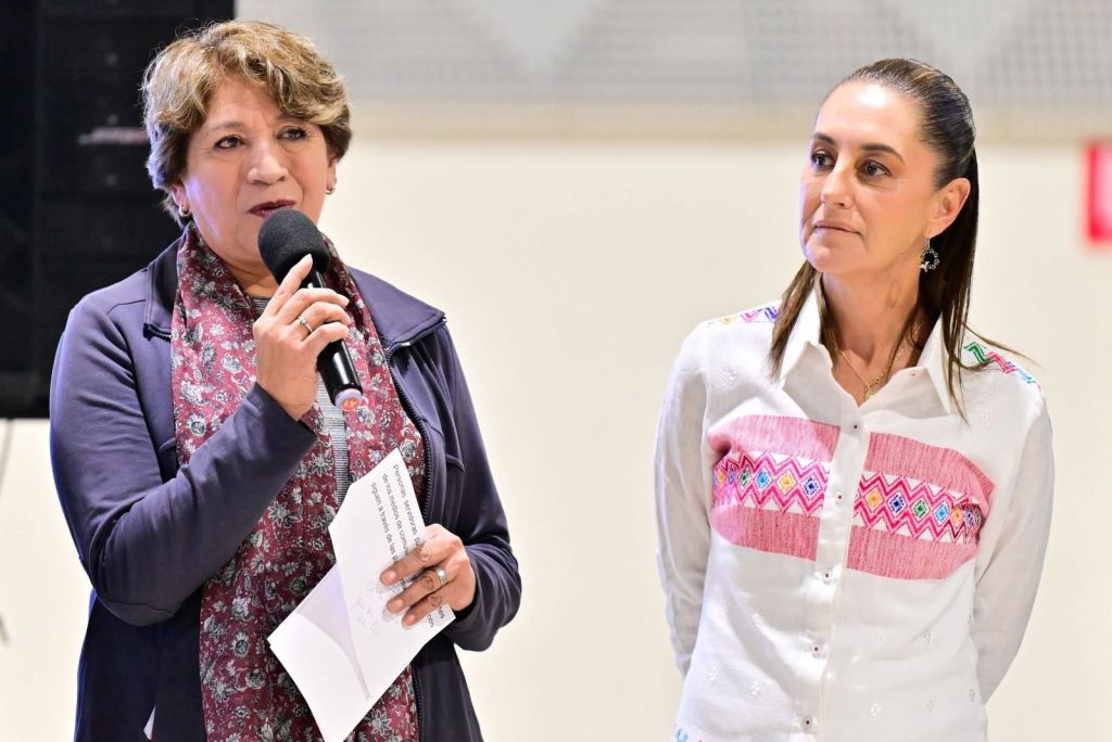 Dos mujeres en un evento, una de ellas habla por un micrófono, la otra escucha atentamente.