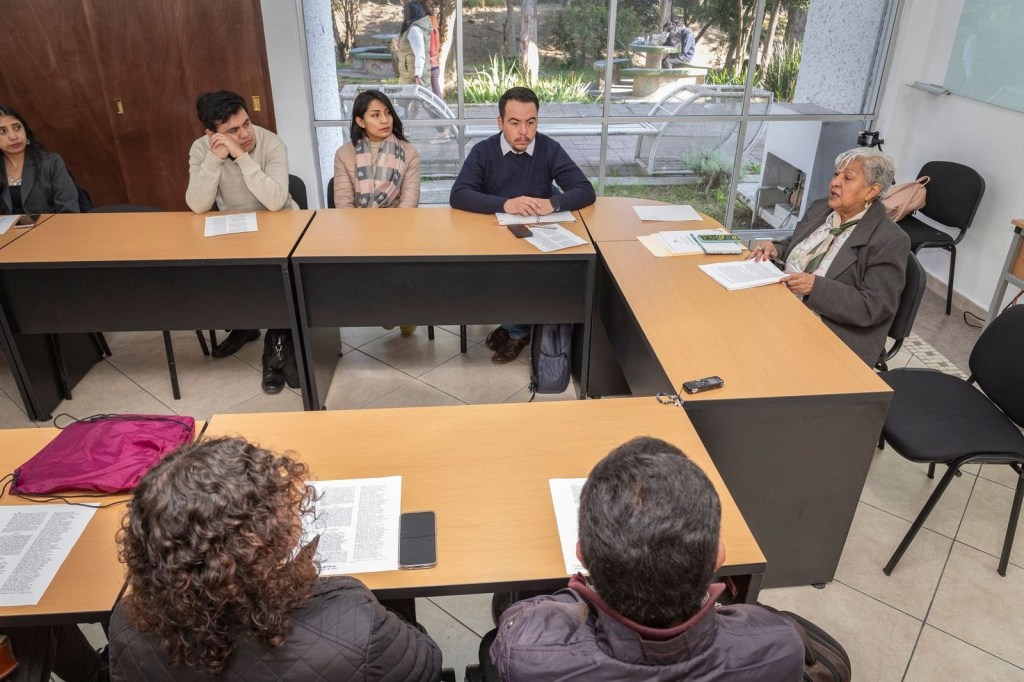 Un grupo de personas se sienta en torno a una mesa de discusión, con documentos y notas frente a ellos, en un ambiente académico.