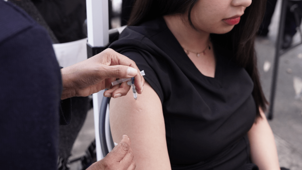 A health professional administering a vaccination to a woman’s arm in a clinical setting.