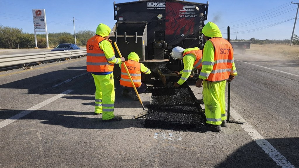 Trabajadores de la construcción realizando reparación de pavimento en una carretera, usando equipos y materiales asfálticos.