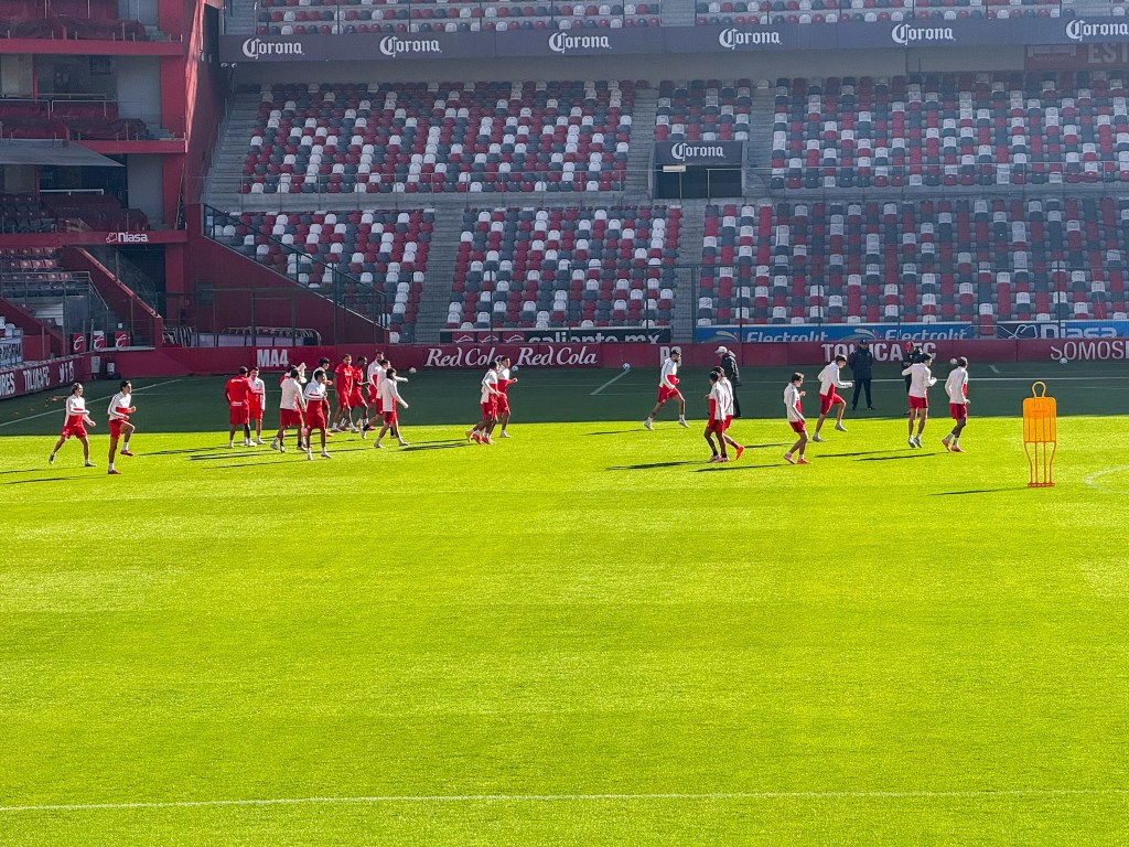 Jugadores del Toluca FC entrenando en el Estadio Nemesio Diez, con el césped bien cuidado y la tribuna vacía de fondo.