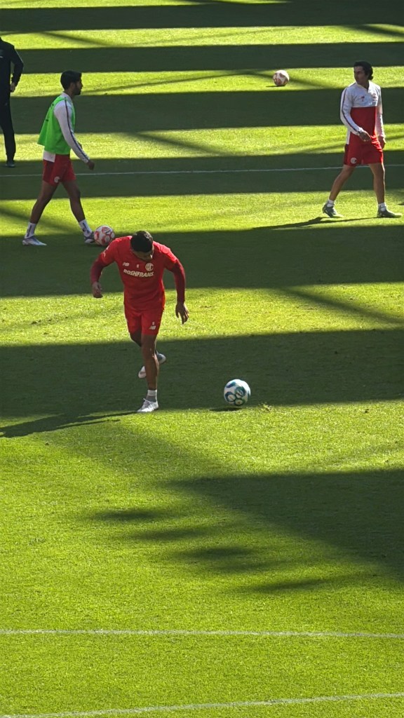 Jugadores del Toluca FC entrenando en el Estadio Nemesio Diez, con luz natural y sombras sobre el campo.