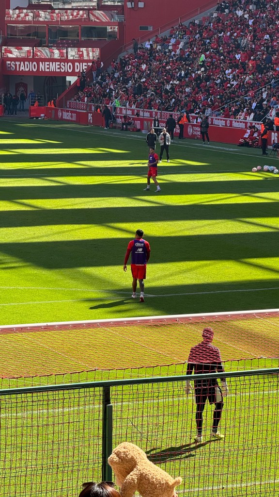 Entrenamiento de futbol en el Estadio Nemesio Diez con afición en las gradas, un jugador en el campo y un portero de espaldas.