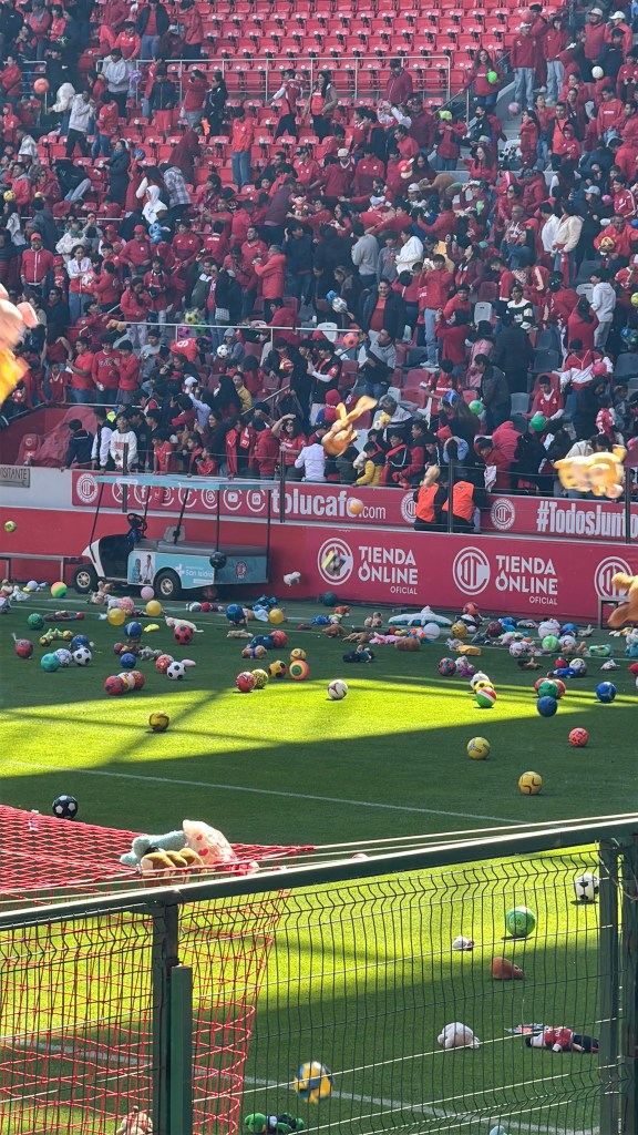Vista del Estadio Nemesio Diez lleno de aficionados del Toluca FC, lanzando peluches y balones al campo durante un evento benéfico por el Día de Reyes.