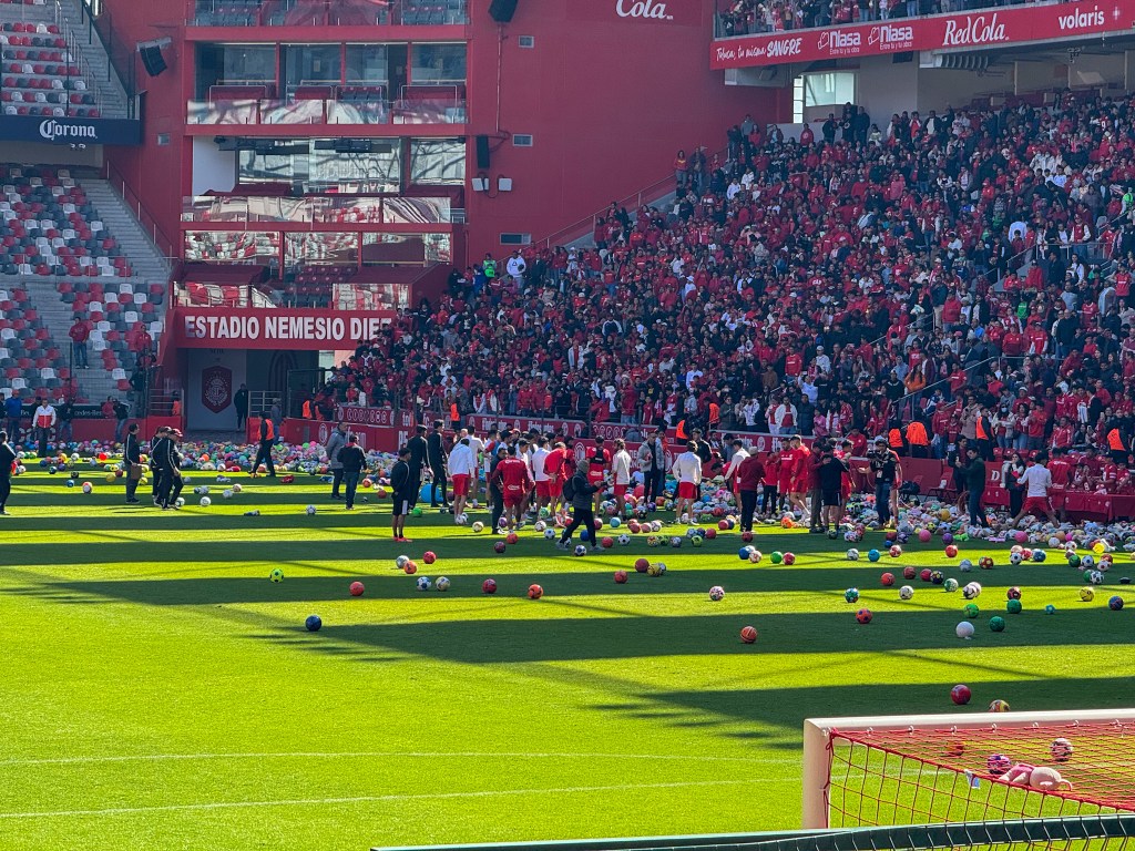 El Estadio Nemesio Diez lleno de aficionados del Toluca FC durante un entrenamiento especial, con pelotas de futbol y donaciones de juguetes esparcidas en el campo.