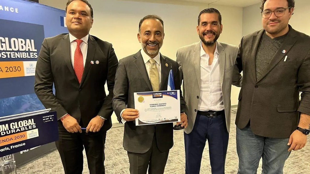 Four men posing for a photo, with one man holding a certificate. The background features a banner with 'Forum Global Sostenibles' and 'Agenda 2030'.
