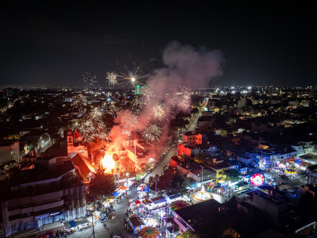 Vista nocturna de una ciudad con fuegos artificiales iluminando el cielo, un evento festivo con luces brillantes y una multitud en las calles.