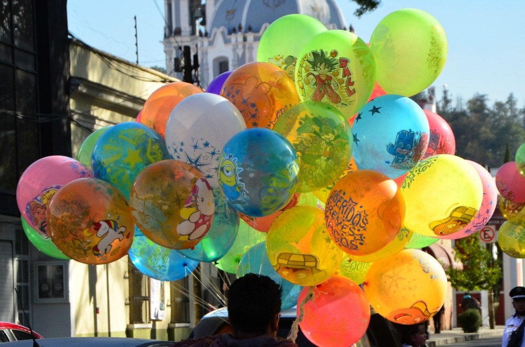Un grupo de globos coloridos con personajes animados, sostenidos por una persona, en un entorno urbano.