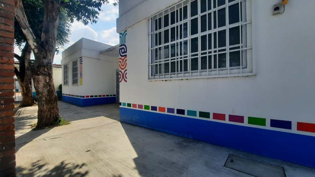View of a colorful wall and pathway leading to a building with large windows, surrounded by trees.