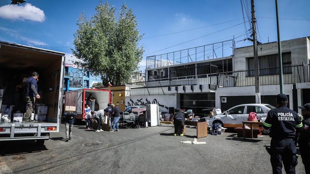Operativos de desalojo en una calle con camiones de mudanza y presencia policial, donde se observa a varias personas sacando muebles y objetos en una zona urbana.
