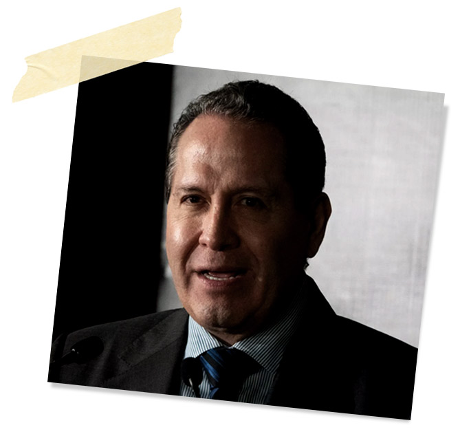 Hombre hablando en un micrófono, con fondo oscuro y luz tenue que ilumina su rostro.