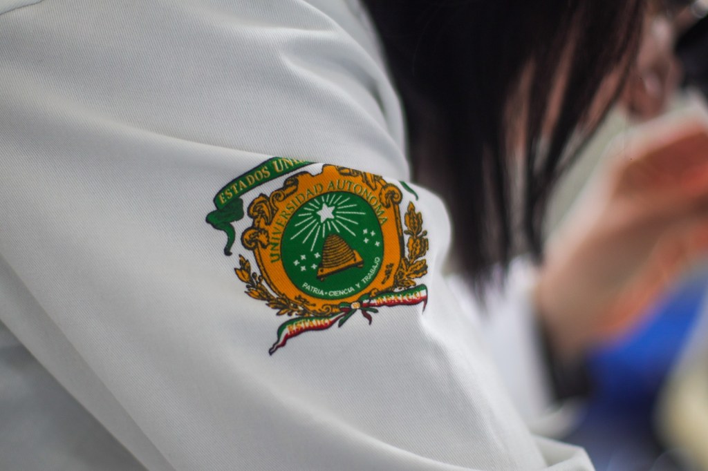 Close-up of a person's sleeve featuring an embroidered university emblem with the text 'Estados Unidos Mexicanos' and 'Universidad Autónoma'.