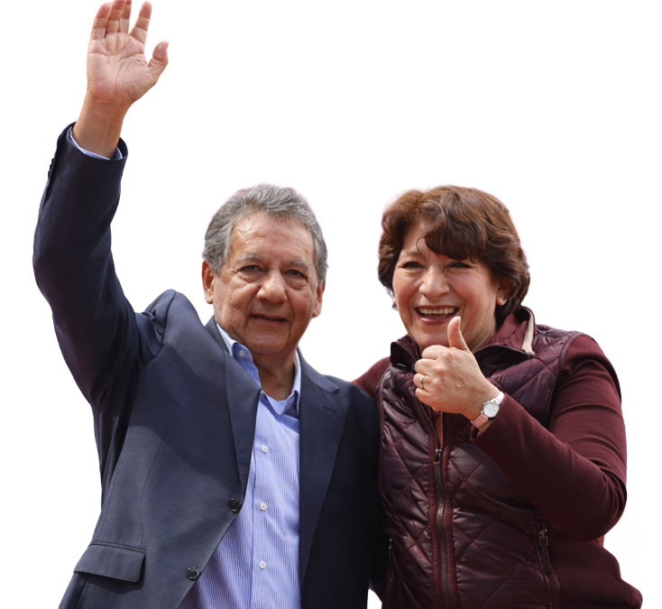 Dos personas sonriendo y saludando, una con la mano levantada y la otra con el pulgar hacia arriba, en un evento público.