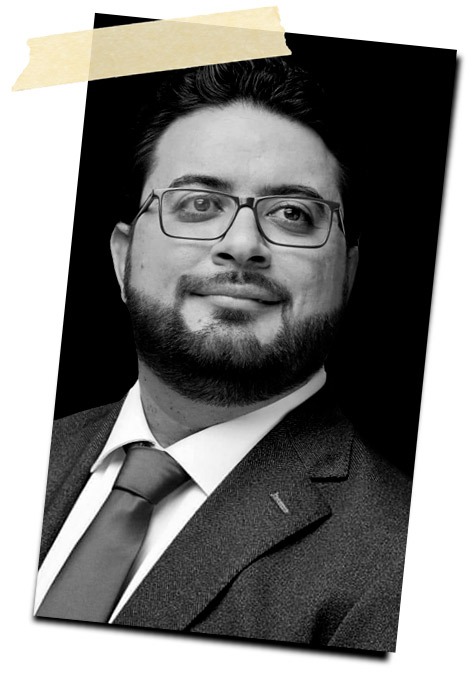 Retrato en blanco y negro de un hombre con barba, usando gafas y un traje oscuro, sonriendo levemente.