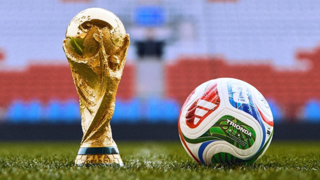 Trofeo de la Copa del Mundo de la FIFA junto a un balón de fútbol en el campo.