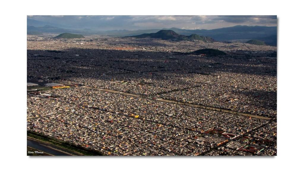 Vista aérea de una ciudad extensa con numerosas edificaciones, rodeada de montañas y un río visible en la parte inferior.