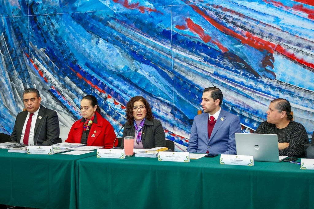 A group of five individuals seated at a conference table, discussing matters, with a large colorful abstract mural in the background.