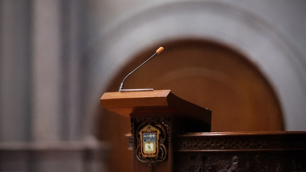 A wooden podium with a microphone in a formal setting, featuring a decorative emblem on the side.