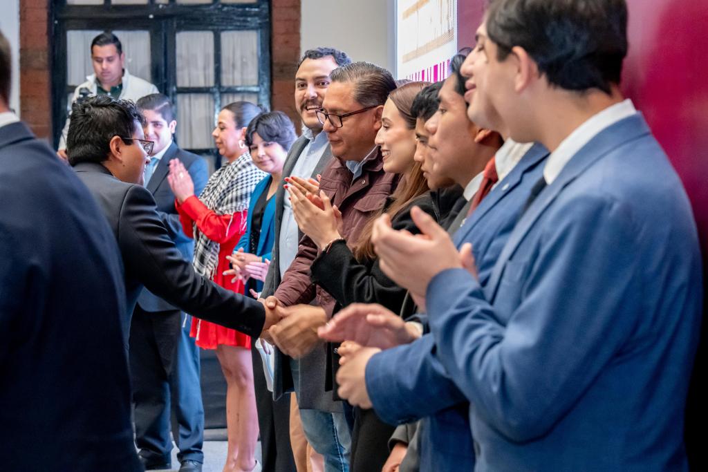 A group of professionals shaking hands and applauding at an event, with a mix of men and women dressed in business attire.